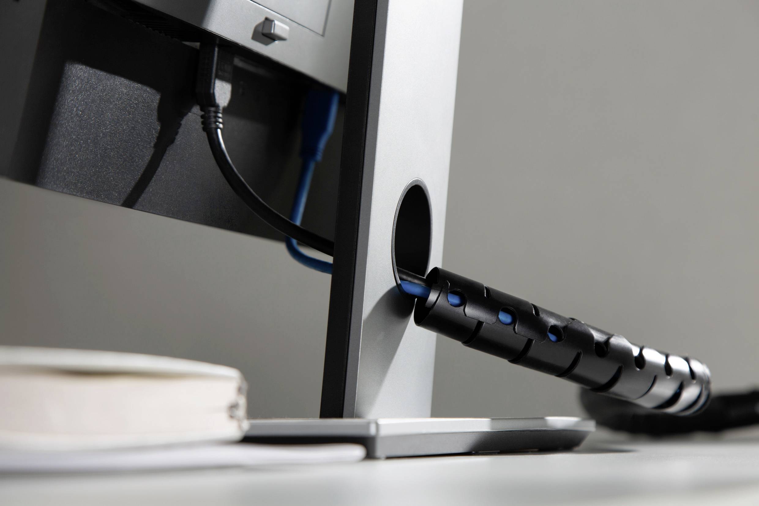 Ein Computermonitor mit Kabelmanagement beim Kabelausgang. Im Vordergrund ist unscharf ein Notizbuch sichtbar.