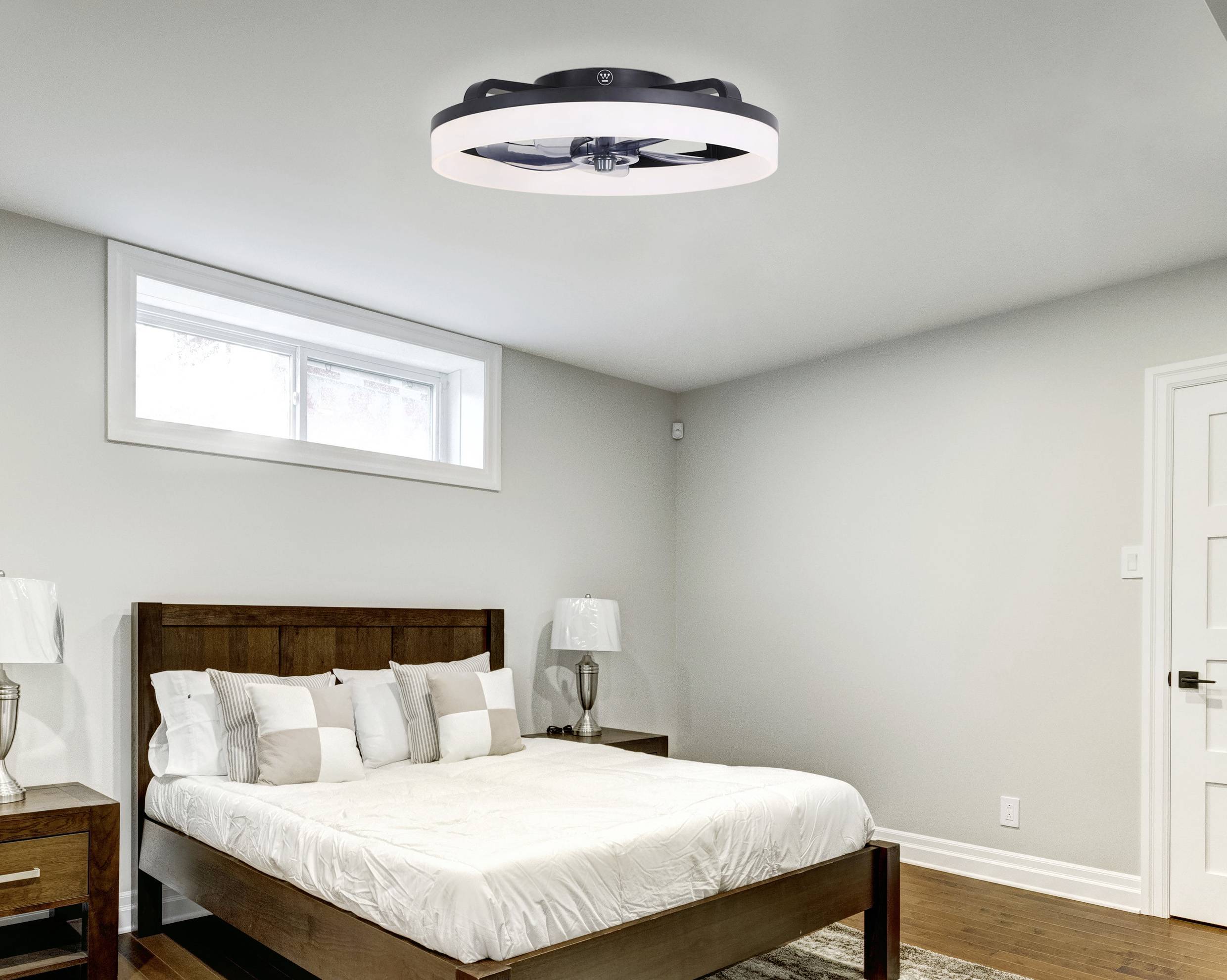 Schlafzimmer mit einem großen Bett, Holzmöbeln und einem modernen Deckenventilator. Ein Fenster lässt Tageslicht herein.