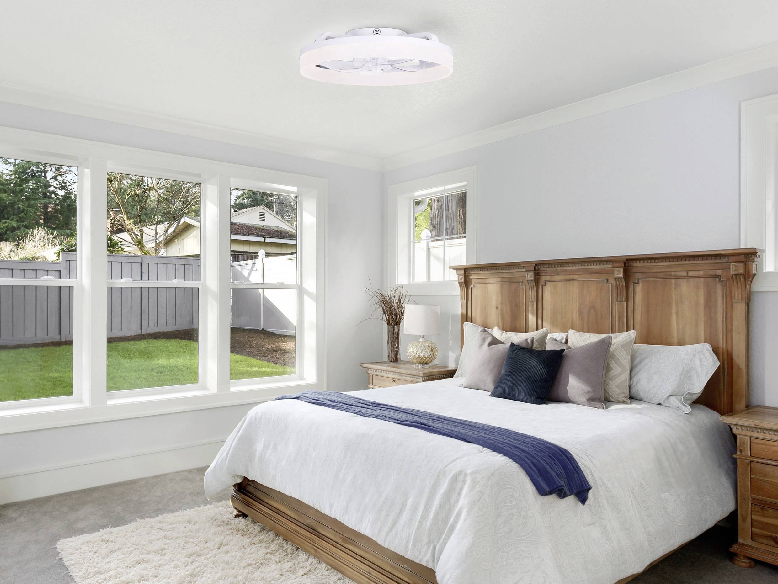 Helles Schlafzimmer mit großem Bett, Holzmöbeln, weißen Wänden und großem Fenster mit Blick auf einen Garten.