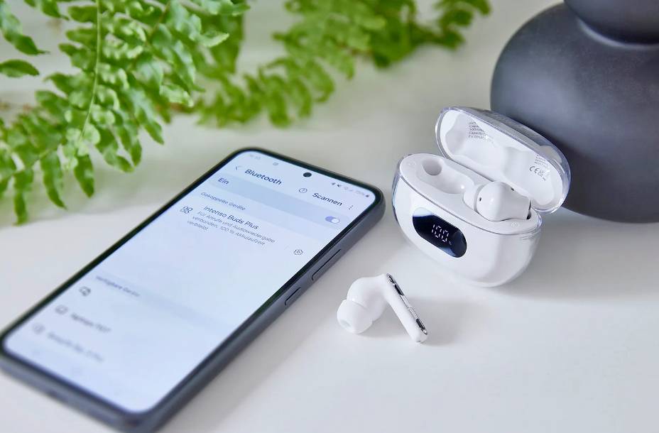 Smartphone neben weißem kabellosen Earbuds-Set in geöffneter Ladehülle auf Tisch; Bluetooth-Verbindung wird auf dem Handy angezeigt.