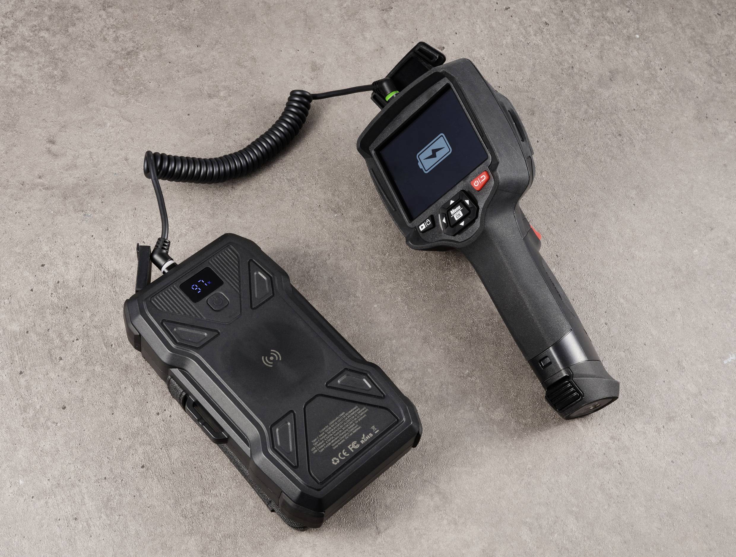 Ein tragbares Infrarot-Thermometer mit angeschlossenem Kabel und digitalem Bildschirm liegt neben einem Gehäuse auf einer grauen Oberfläche.