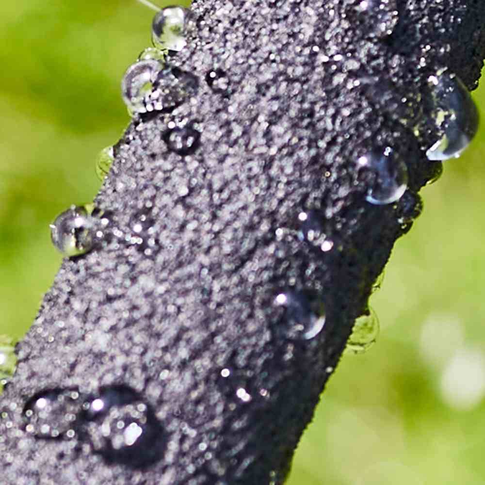 Wassertropfen auf einem dunklen, strukturierten Ast in Nahaufnahme, umgeben von grünem Hintergrund.