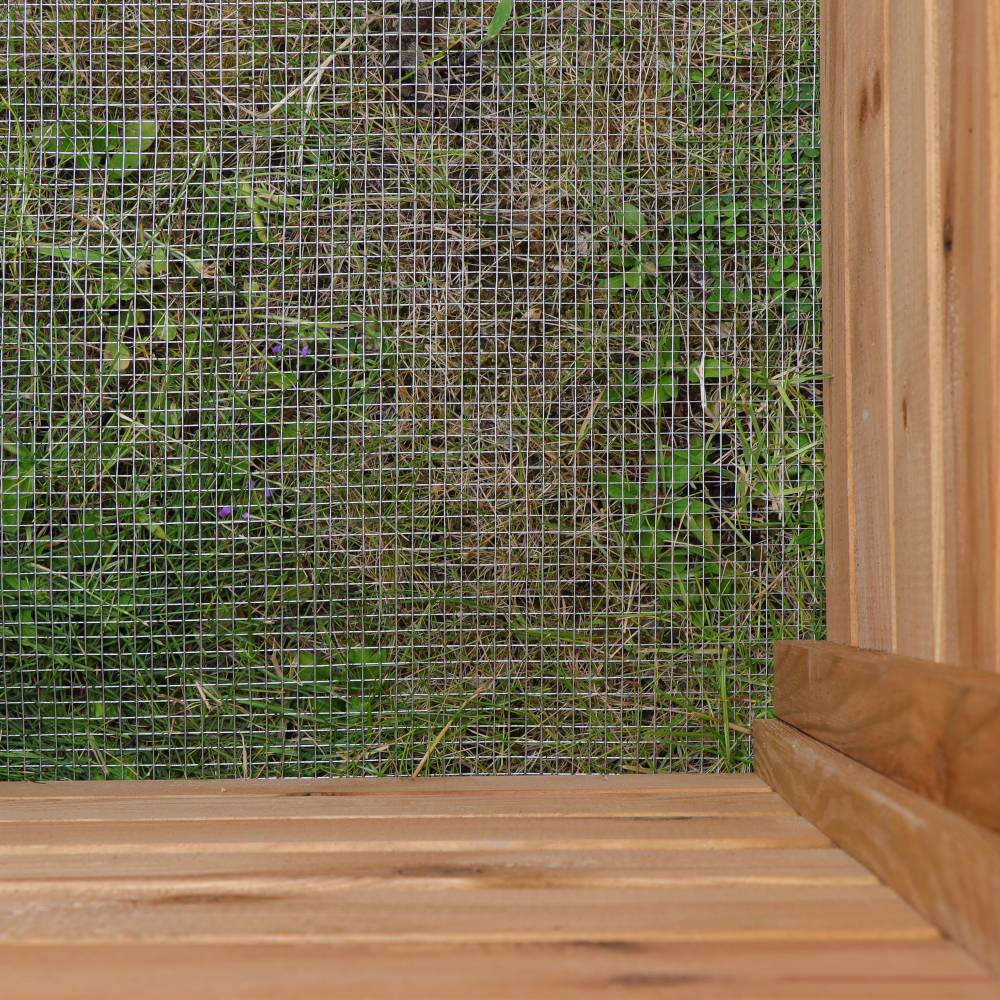 Blick durch ein Gitter auf Gras, begrenzt durch eine Holzwand und -boden. Hauptthema ist die Abgrenzung zwischen Natur und Struktur.