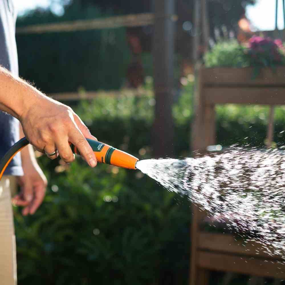Eine Person gießt Pflanzen mit einem Gartenschlauch in einem sonnigen Garten.