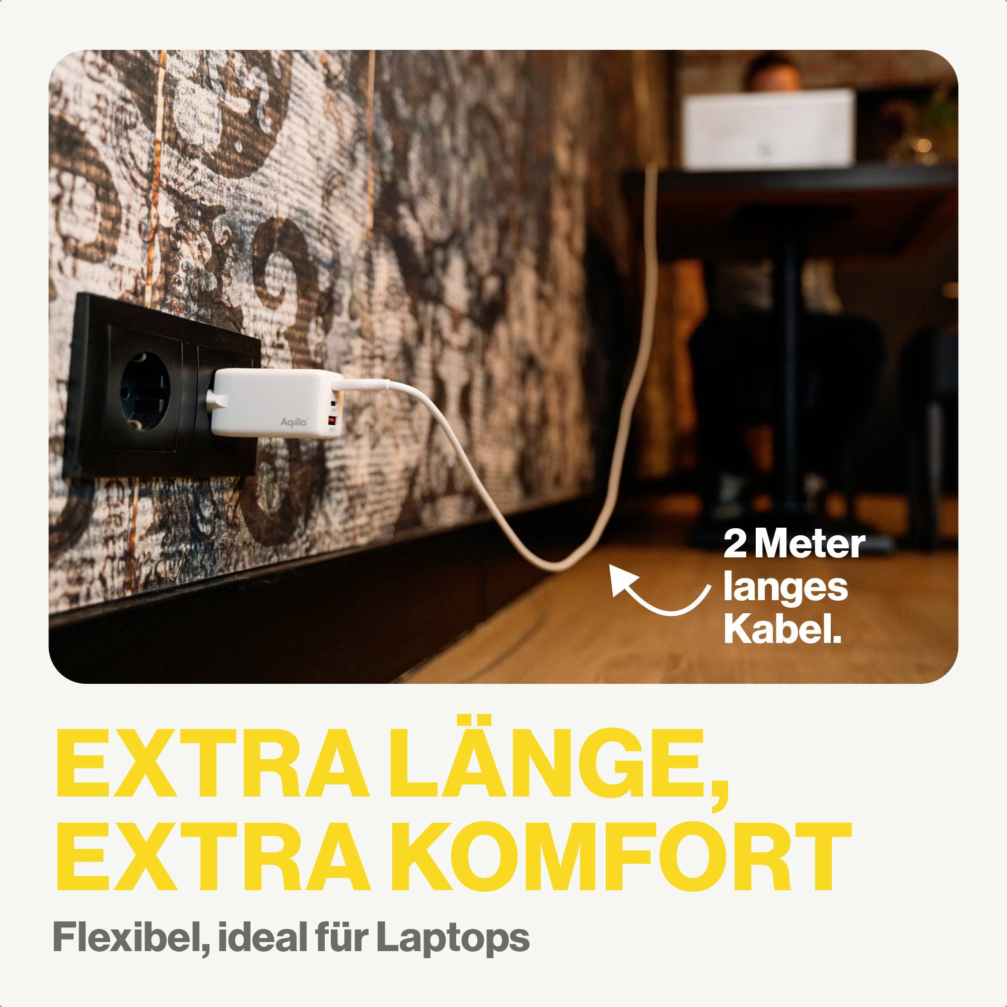 Ladesystem mit 2 Meter langem Kabel an Wandsteckdose für Laptops; Bild zeigt Person, die an einem Tisch arbeitet. Text: 'EXTRA LÄNGE, EXTRA KOMFORT. Flexibel, ideal für Laptops'.