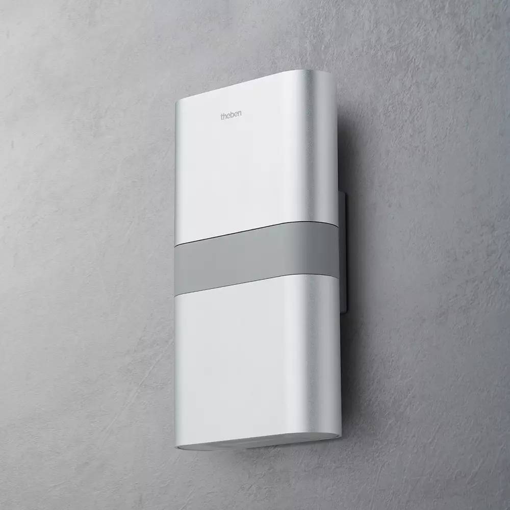 Weiße rechteckige Außenleuchte mit grauem Band, montiert an einer grauen Wand.