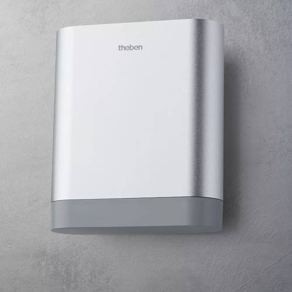 Ein silbernes und graues rechteckiges Gerät mit der Aufschrift 'theben', an einer grauen Wand montiert.