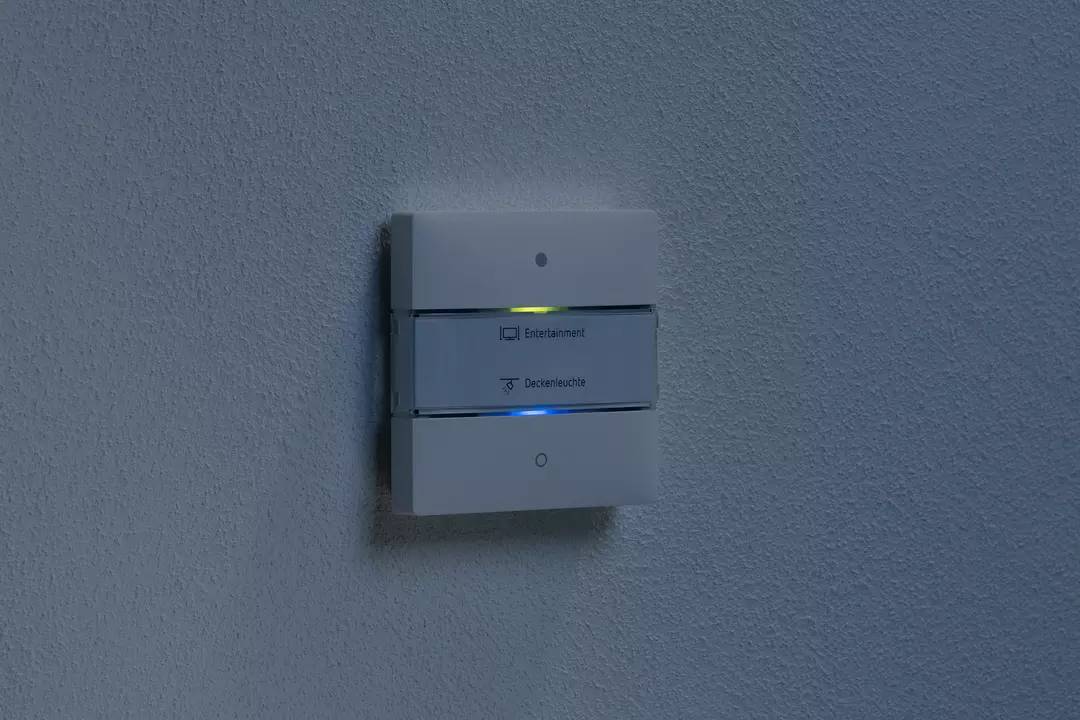 Ein Schalter an der Wand mit leuchtenden Tasten für 'Entertainment' oben und 'Deckenlicht' unten.