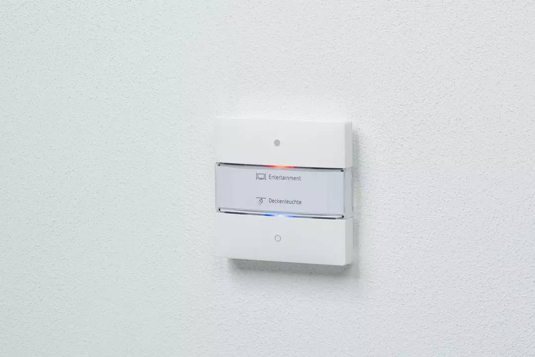 Ein Wandpaneel mit Touchscreen zur Steuerung von 'Entertainment' und 'Deckenleuchte'. Zwei Schaltflächen sichtbar, jeweils mit Symbol.