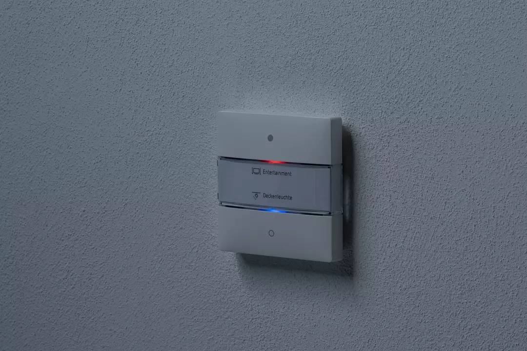 Lichtschalter an einer Wand mit zwei Knöpfen. Der obere Knopf ist mit 'Entertainment' und der untere mit 'Deckenleuchte' beschriftet.