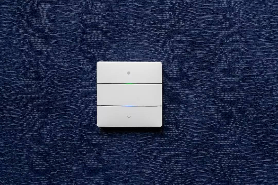 Weißer Wandschalter mit drei horizontalen Tasten, angezeigt auf einer dunkelblauen Textur. Obere Taste hat ein grünes Licht, die mittlere ein blaues.