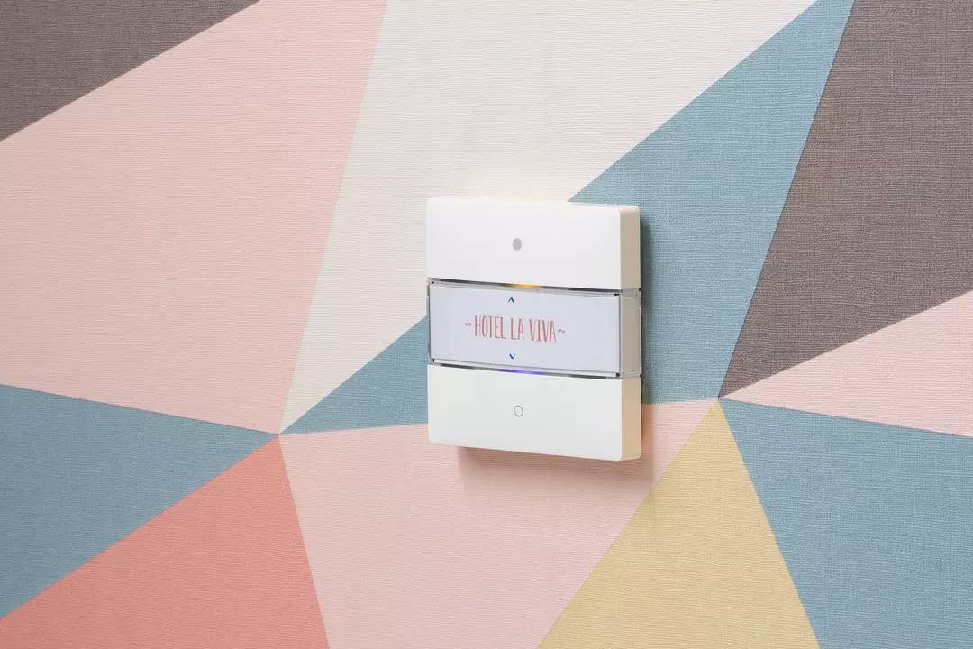 Ein Lichtschalter an einer bunten Wand mit geometrischen Formen. Der Schalter trägt die Aufschrift 'Hotel La Viva'.