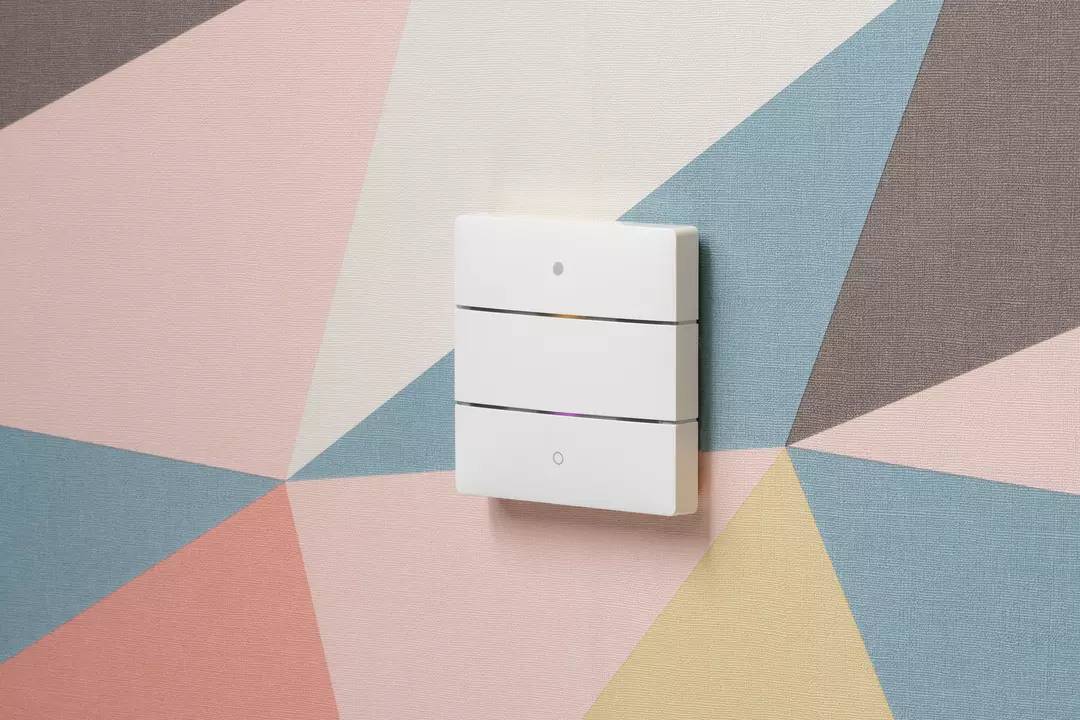 Ein weißer Lichtschalter mit drei horizontalen Linien vor einer farbenfrohen, geometrischen Wandtapete.