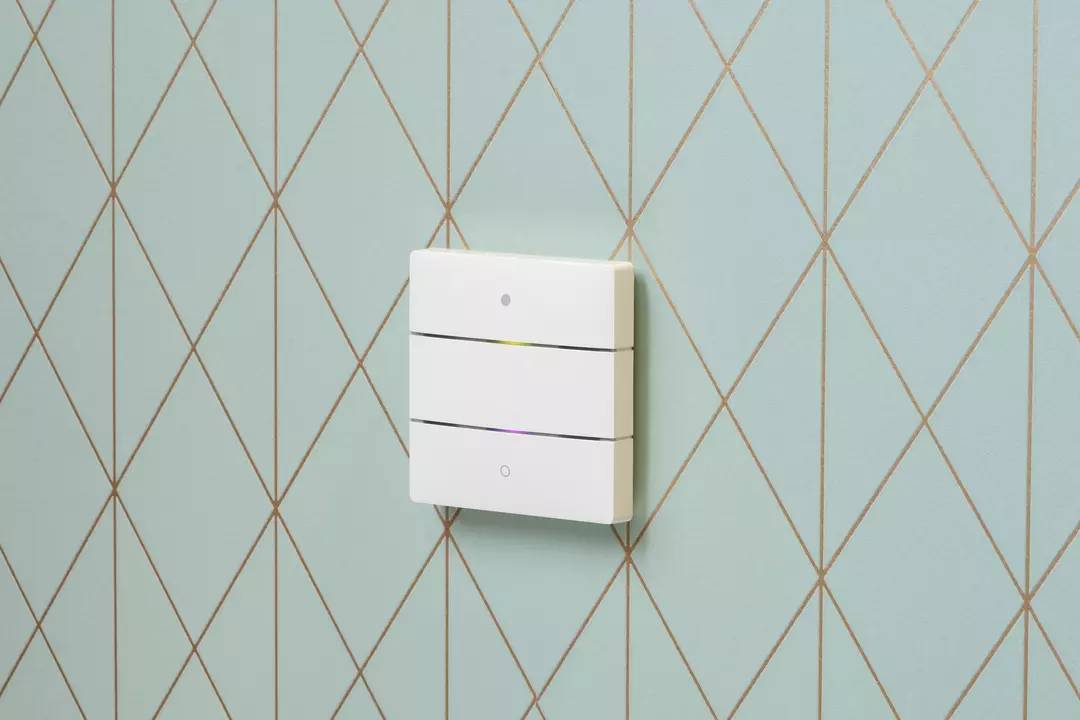 Ein moderner dreifacher Lichtschalter mit grünlichem Hintergrund und goldenen Gitterlinien, an einer Wand montiert.