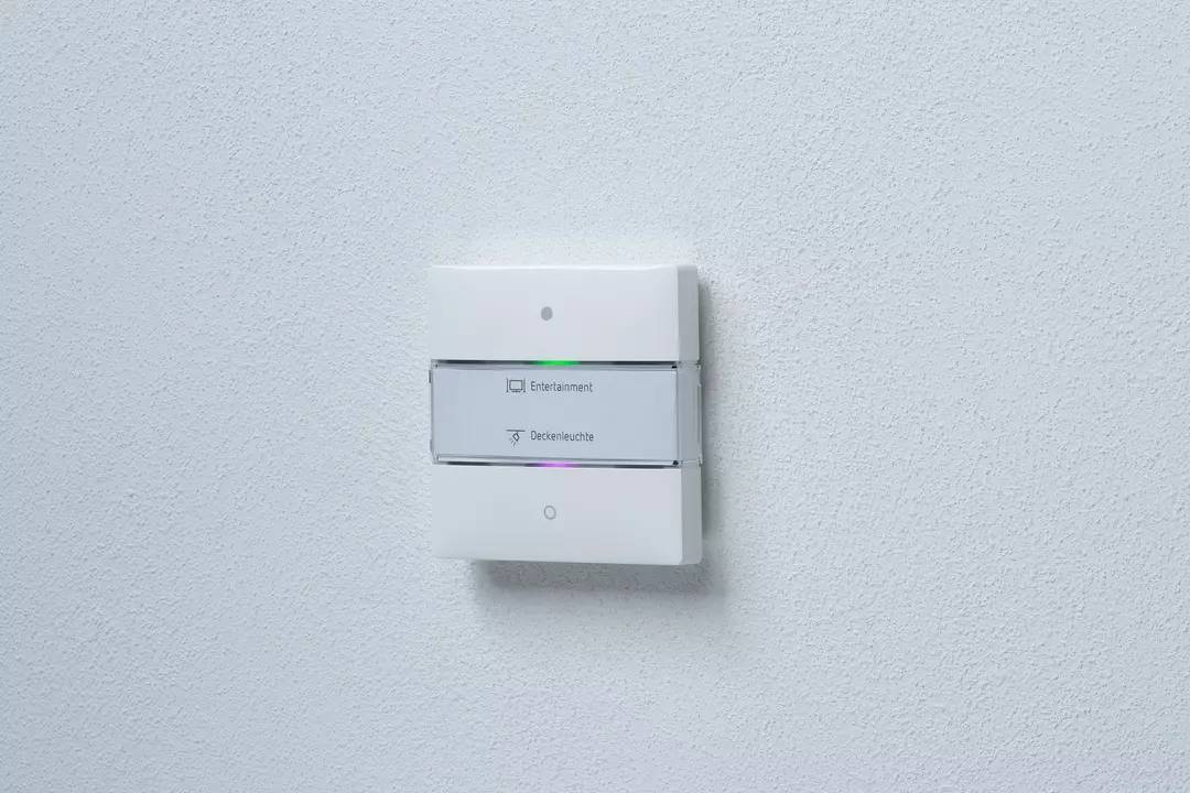 Lichtschalter mit zwei Tasten und kleinen Symbolen darauf: 'Ententasten' und 'Deckenleuchte' in einem weißen Rahmen an einer weißen Wand.