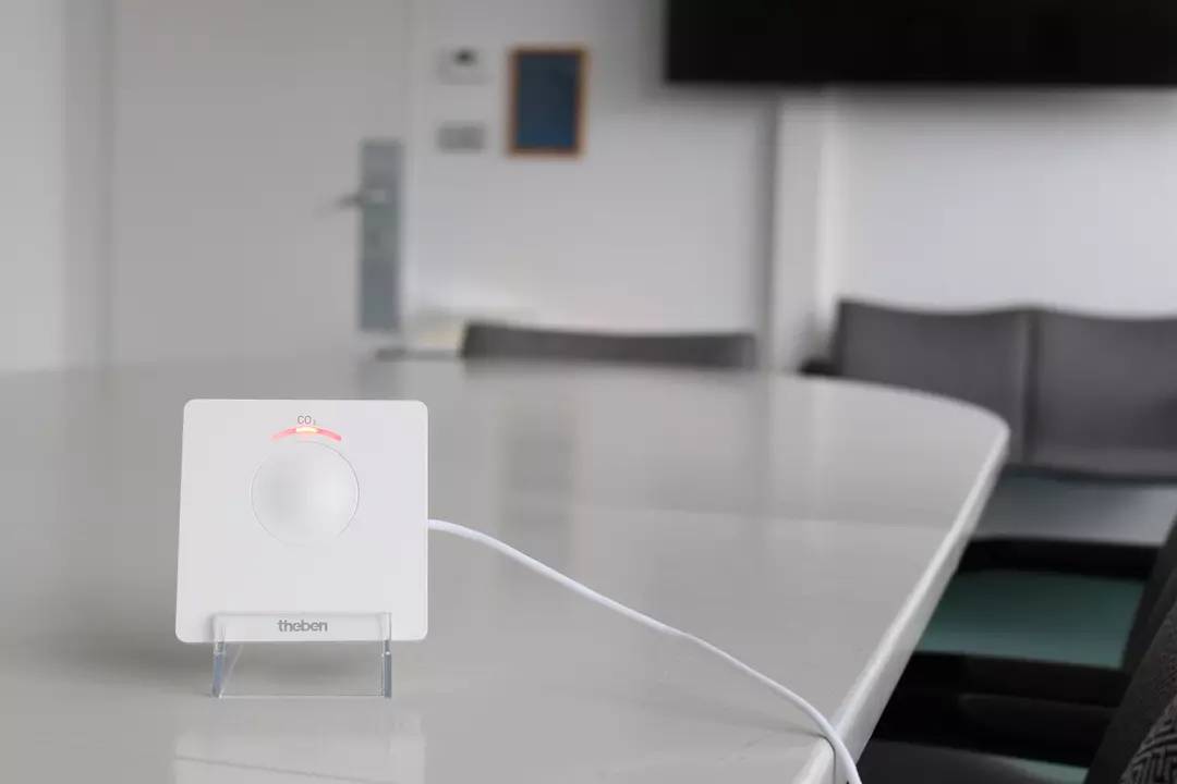 Ein weißer Thermostatregler auf einem Tisch in einem Büro. Der Regler zeigt eine Einstellung von 'Comfort' an.