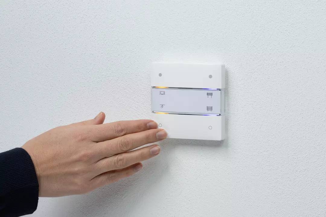Hand betätigt an der Wand einen weißen Lichtschalter mit mehreren Funktionen.