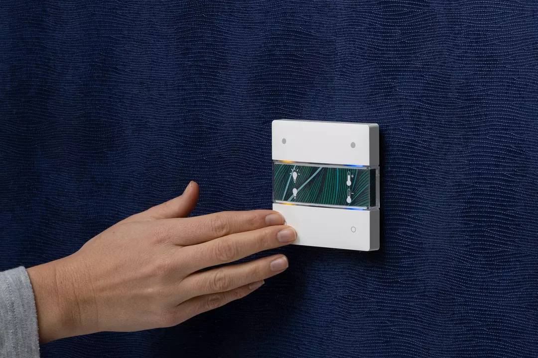 Eine Hand berührt einen modernen Lichtschalter mit digitalem Display auf einer dunkelblauen Wand.