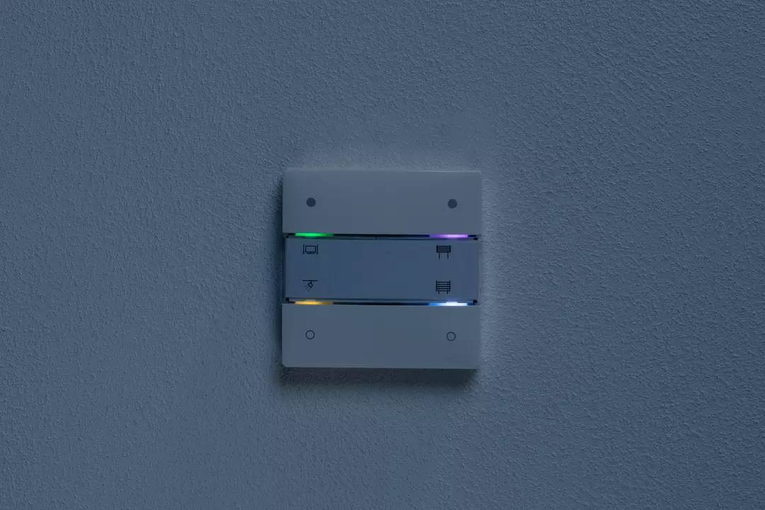 Ein Lichtschalter mit vier Tasten an einer Wand, beleuchtet mit bunten LEDs. Obere Tasten zeigen Symbole für Licht; untere für Jalousien.