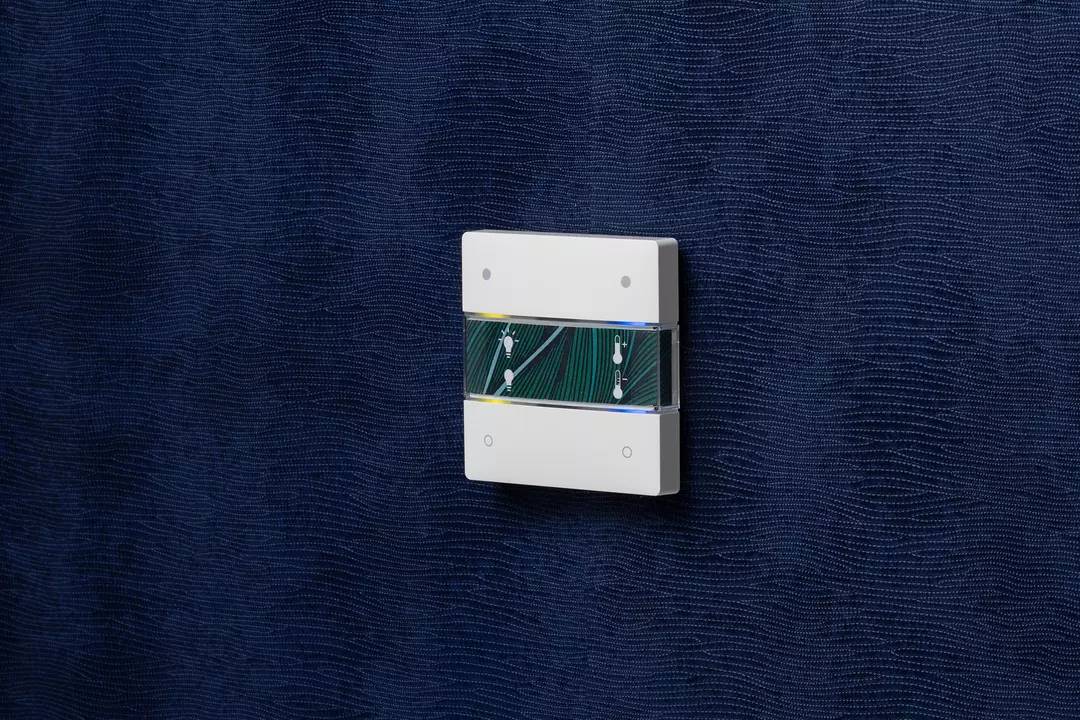 Ein moderner Lichtschalter mit zwei Tasten an einer dunkelblauen Wand.