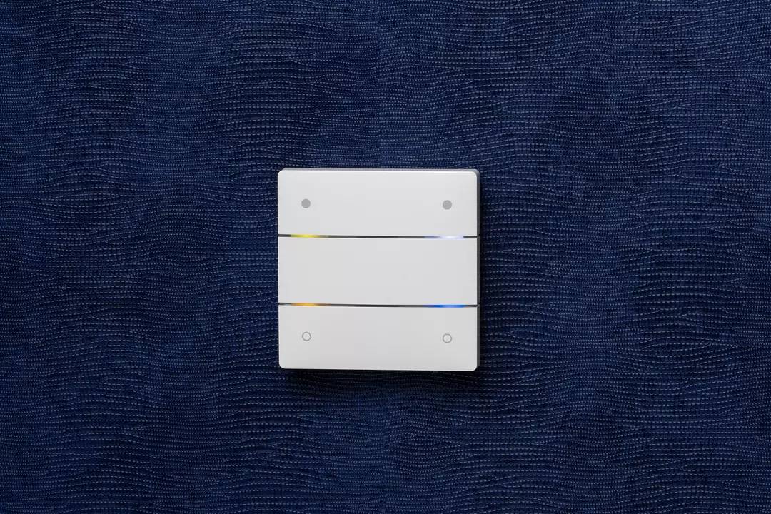 Ein weißer Lichtschalter mit drei Schaltflächen an einer dunkelblauen Wand.
