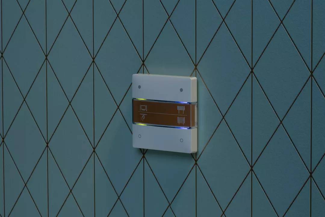 Ein beleuchteter Lichtschalter auf einer gefliesten Wand zeigt Symbole für Licht- und Jalousiensteuerung.
