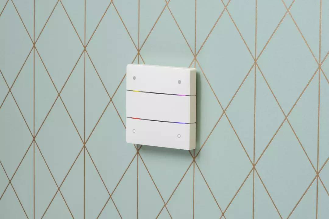 Lichtschalter mit drei horizontalen Streifen an einer türkisfarbenen Tapete mit goldenen Rautenmustern.