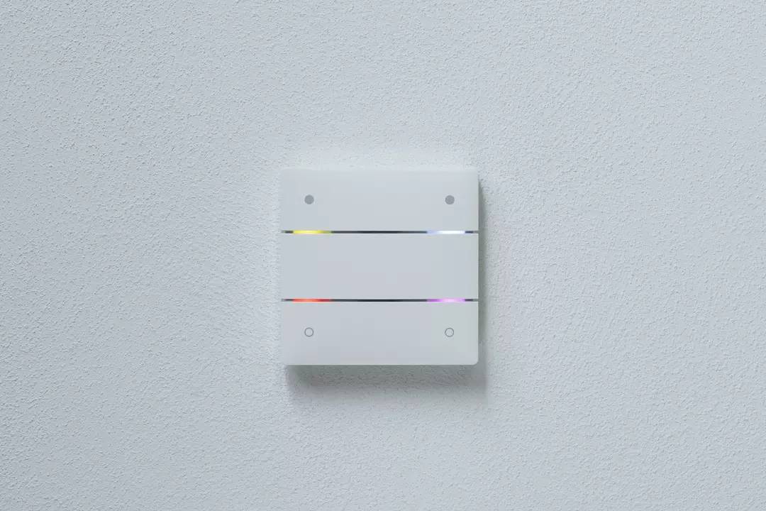 Ein weißer, rechteckiger Lichtschalter an einer Wand mit vier kleinen LEDs in den Ecken, die in verschiedenen Farben leuchten.