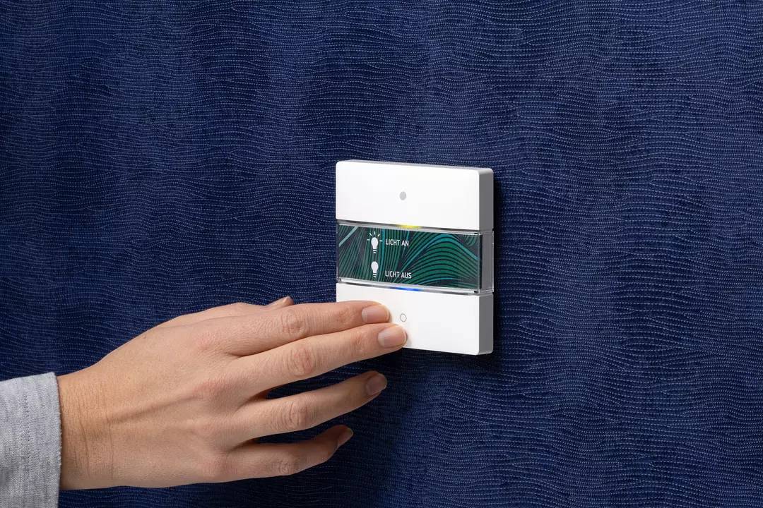 Eine Hand berührt einen Lichtschalter an der Wand. Der Schalter hat zwei Tasten: 'Licht an' und 'Licht aus', in einem modernen Design.
