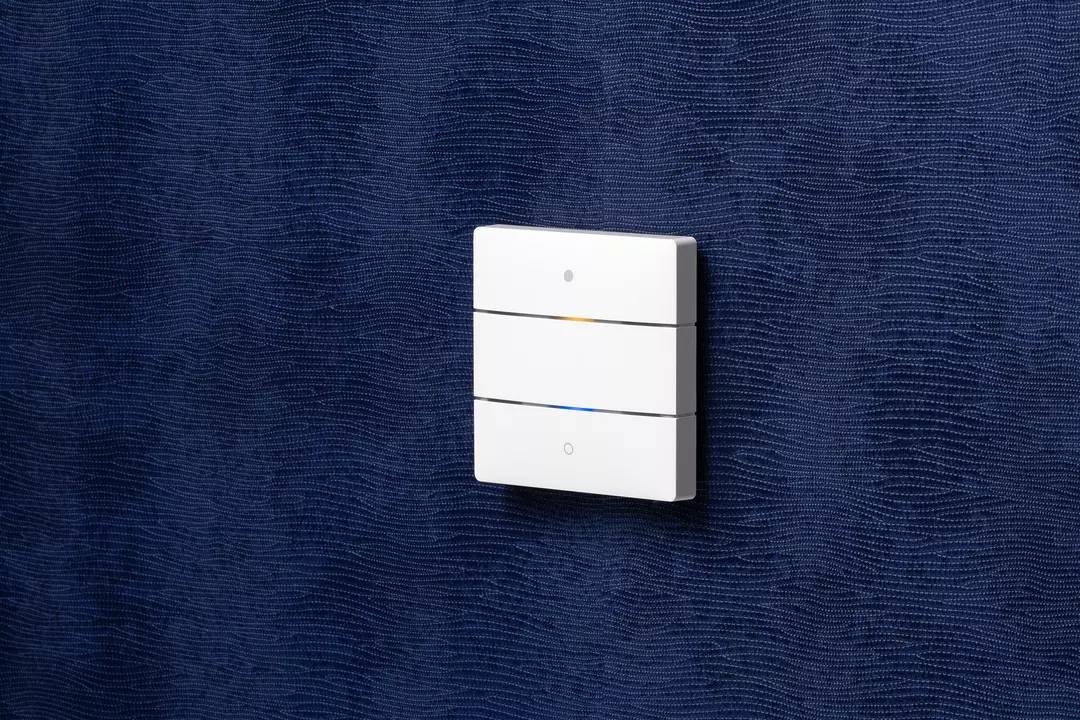 Ein einzelner weißer Lichtschalter mit drei Tasten ist an einer strukturierten, dunkelblauen Wand montiert.