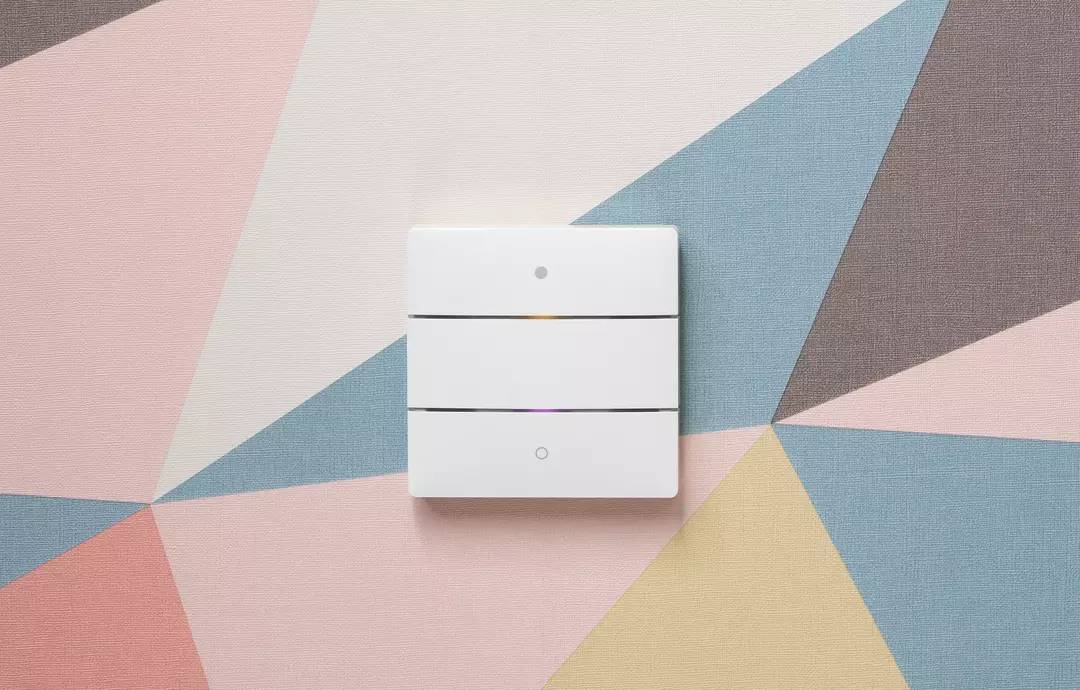 Ein dreiteiliger weißer Lichtschalter an einer Wand mit geometrischem Muster in Pastellfarben.
