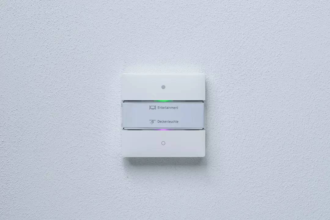 Lichtschalter an der Wand mit zwei Tasten, beschriftet mit 'Entertainment' und 'Deckenleuchte', jeweils mit kleinem Kontrolllicht.