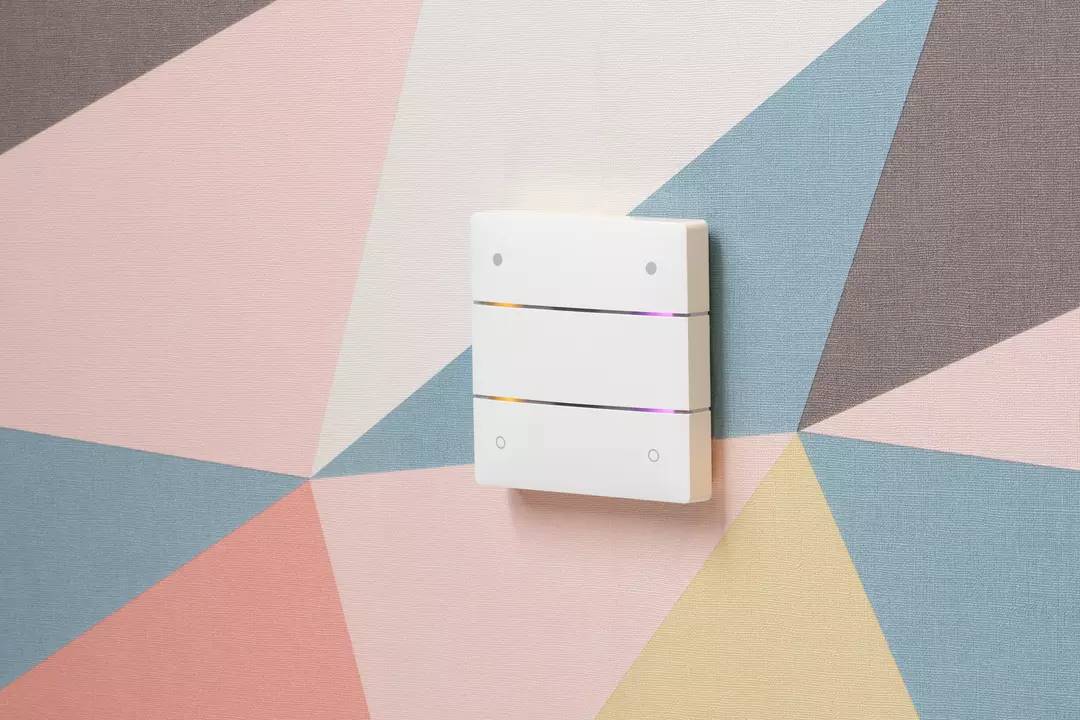 Ein weißer Lichtschalter mit drei horizontalen Linien vor einer bunt gemusterten Wand.