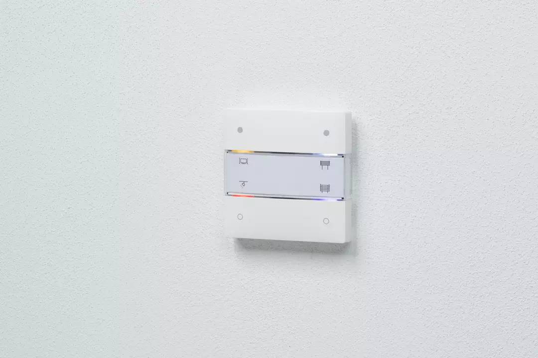 Ein weißer Lichtschalter an einer Wand mit zwei Kippschaltern und symbolischen Markierungen, die auf verschiedene Funktionen hinweisen.