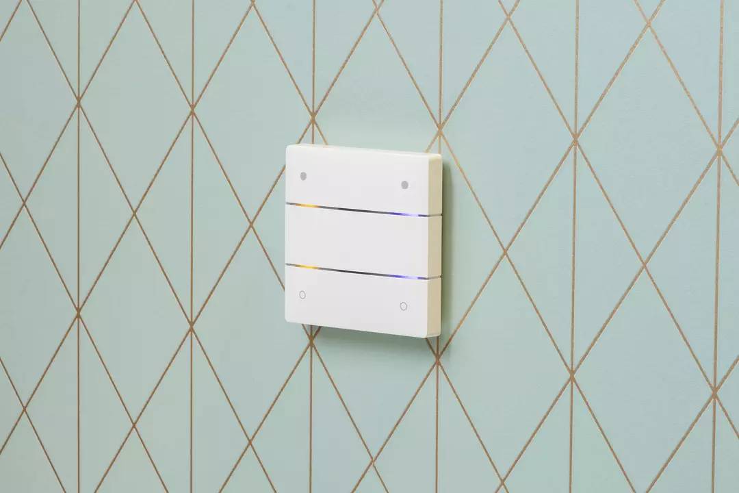 Ein dreiteiliger Lichtschalter an einer türkis-gemusterten Wand, teilweise beleuchtet, zeigt einen modernen, minimalistischen Stil.