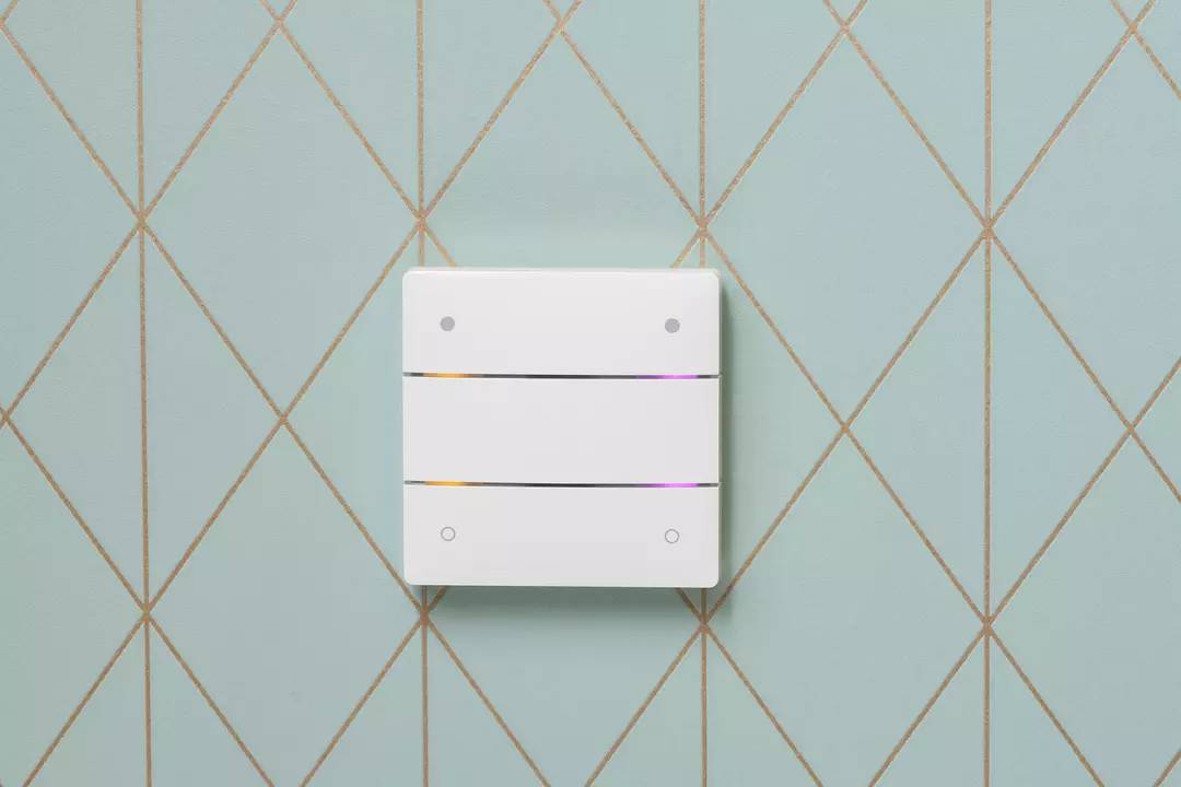 Ein moderner, weißer Lichtschalter an einer blauen Wand mit goldenen Rautenmustern.