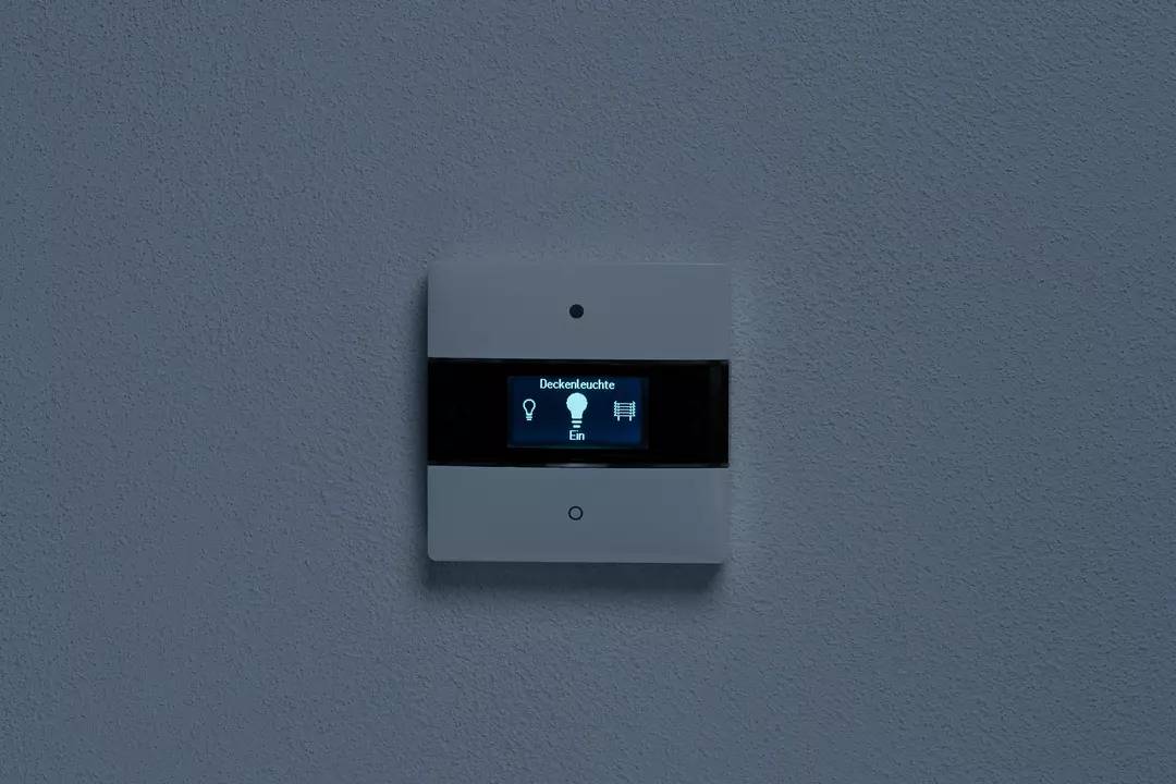 Schalter mit digitalem Display an der Wand, zeigt 'Deckenleuchte Ein'.