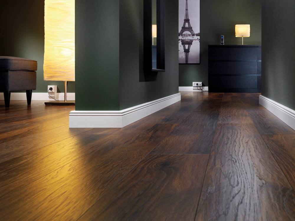 Ein moderner Raum mit dunkelbraunem Holzfußboden, grüne Wände, ein Möbelstück, zwei Lampen und ein Bild des Eiffelturms an der Wand.