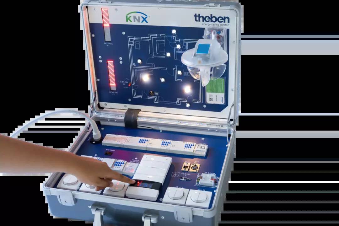 Person demonstriert ein KNX-Schulungskoffer mit Steuerungsmodulen und Lichtanzeigen, verwendet zur Schulung in Gebäudetechnik.
