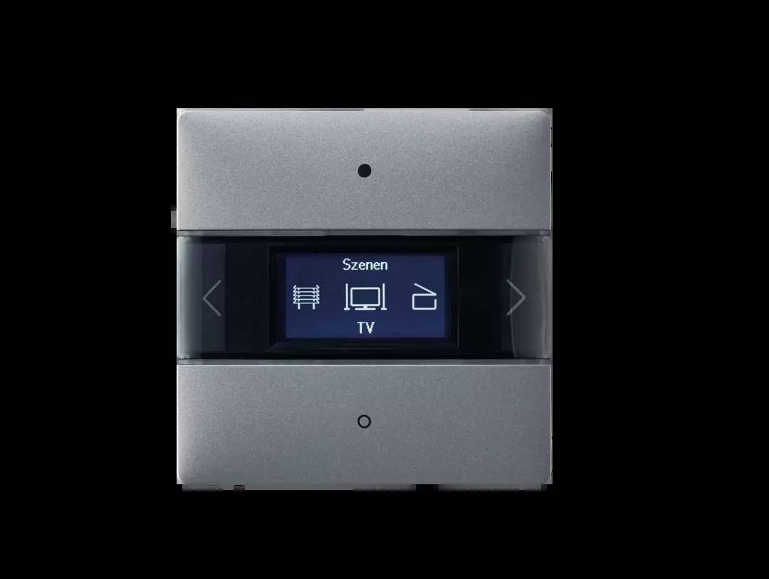 Schalter mit digitalem Display zeigt 'Szenen' Auswahlen: Heizung, TV, Musik. Anzeigen sind mit Pfeilen rechts und links umgeben.