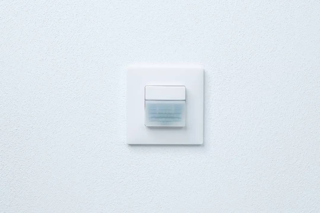 Ein weißer Wandschalter mit einem blauen LED-Licht, in einer schlichten Wand montiert.