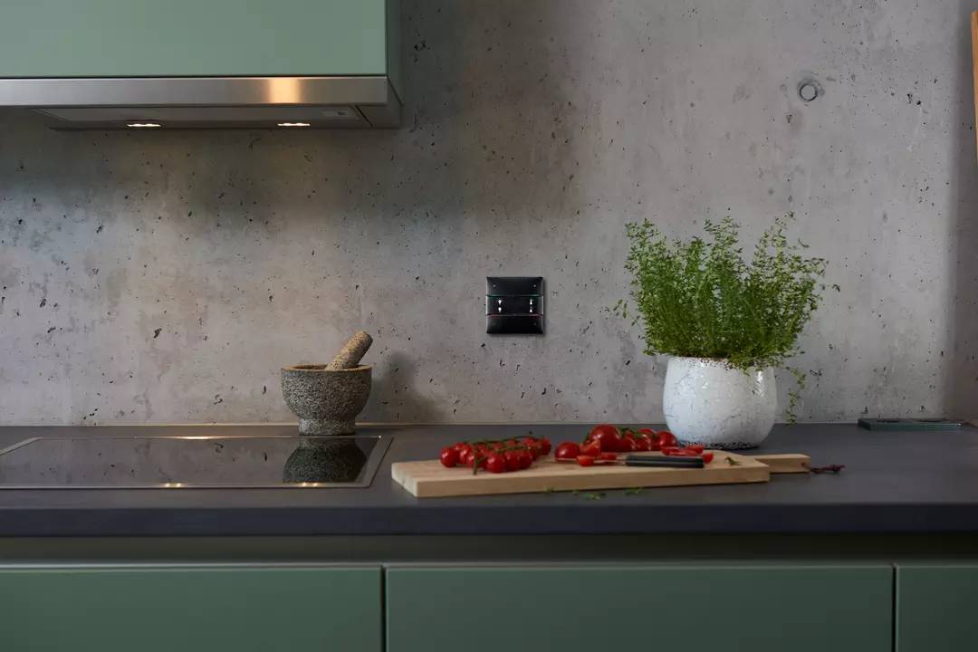 Moderne Küche mit grünem Schrank, Betonwand. Ein Mörser und frische Kräuter stehen neben einem Schneidebrett mit Tomaten.