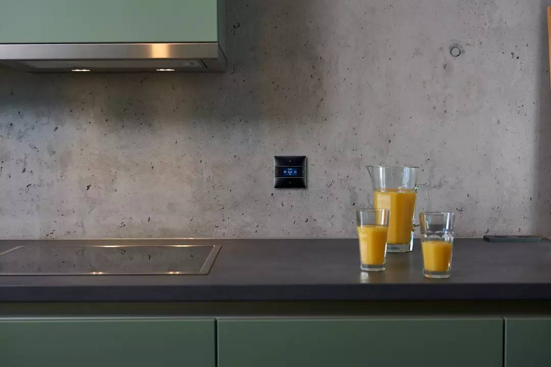 Küchentheke mit drei Gläsern Orangensaft, modernes Kochfeld links, graue Wand im Hintergrund.