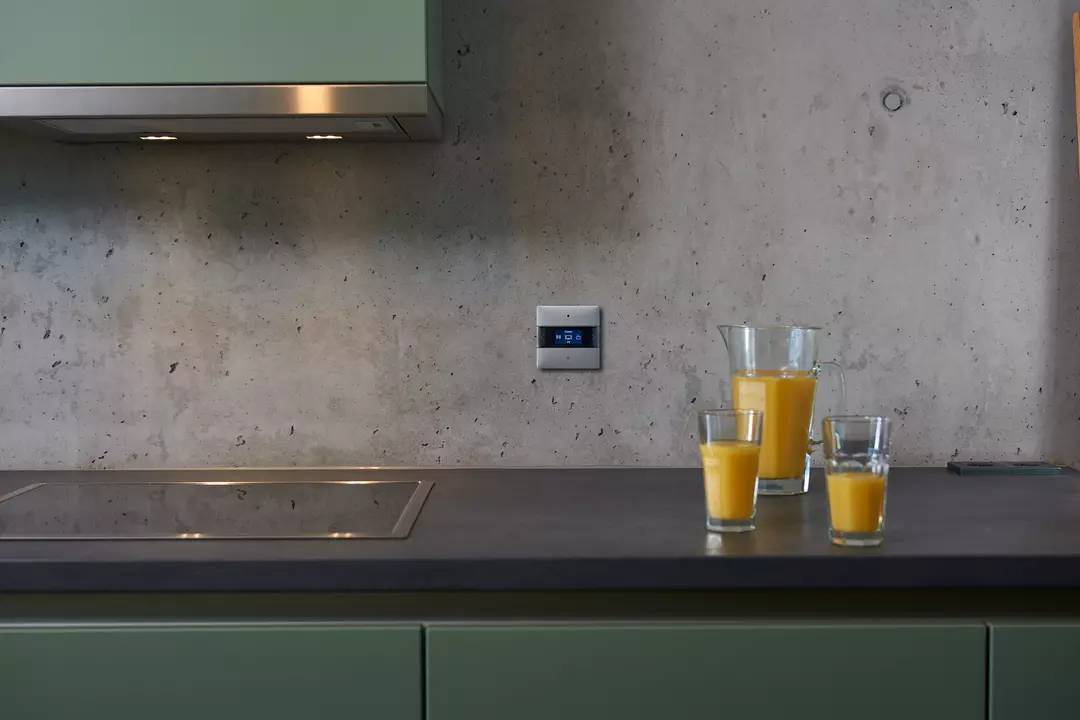 Grüne Küche mit grauer Arbeitsplatte, drei Gläser mit Orangensaft stehen darauf; modernes Ambiente.