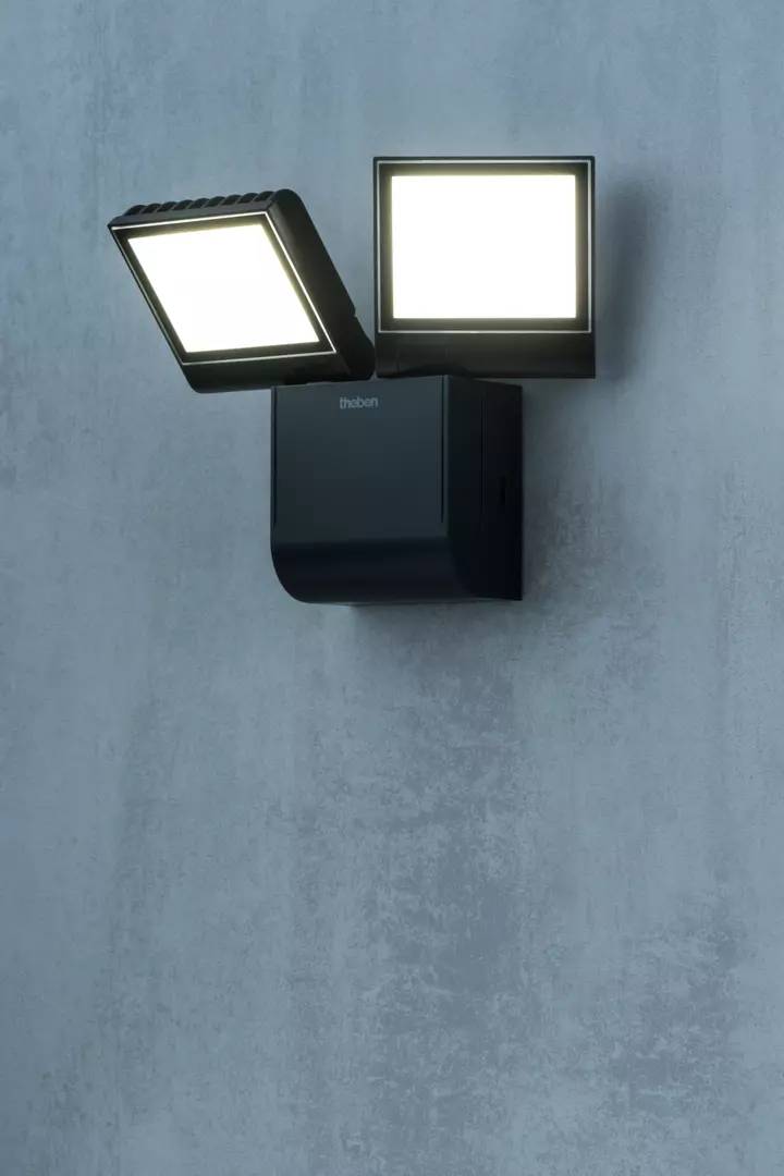 Eine dunkelgraue Außenleuchte mit zwei quadratischen LED-Lampen, die an einer Betonwand montiert ist, leuchtet hell.