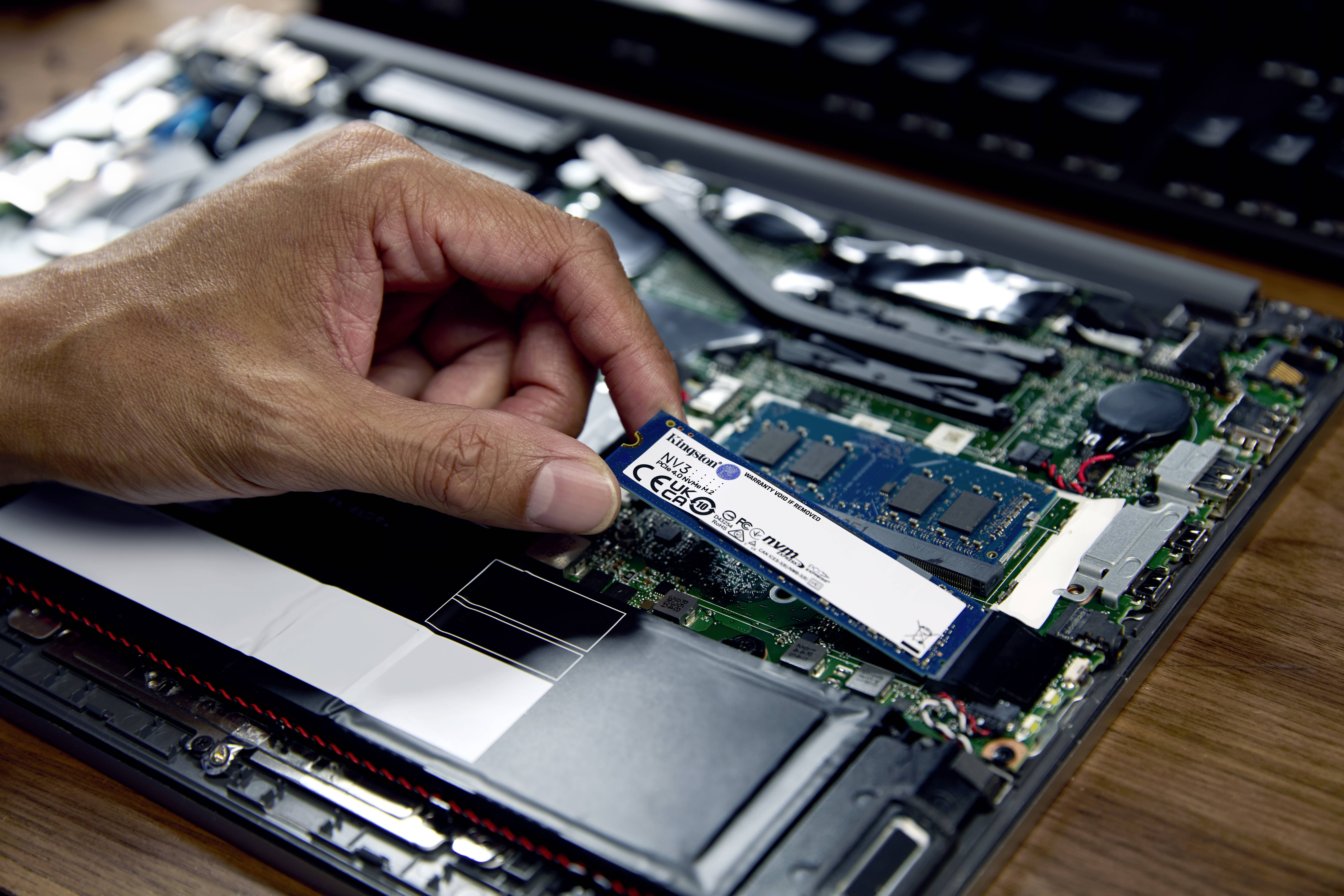Hand setzt eine M.2 SSD in einen Laptop ein, auf einer geöffneten Laptop-Platine mit sichtbarem RAM und anderen Komponenten.