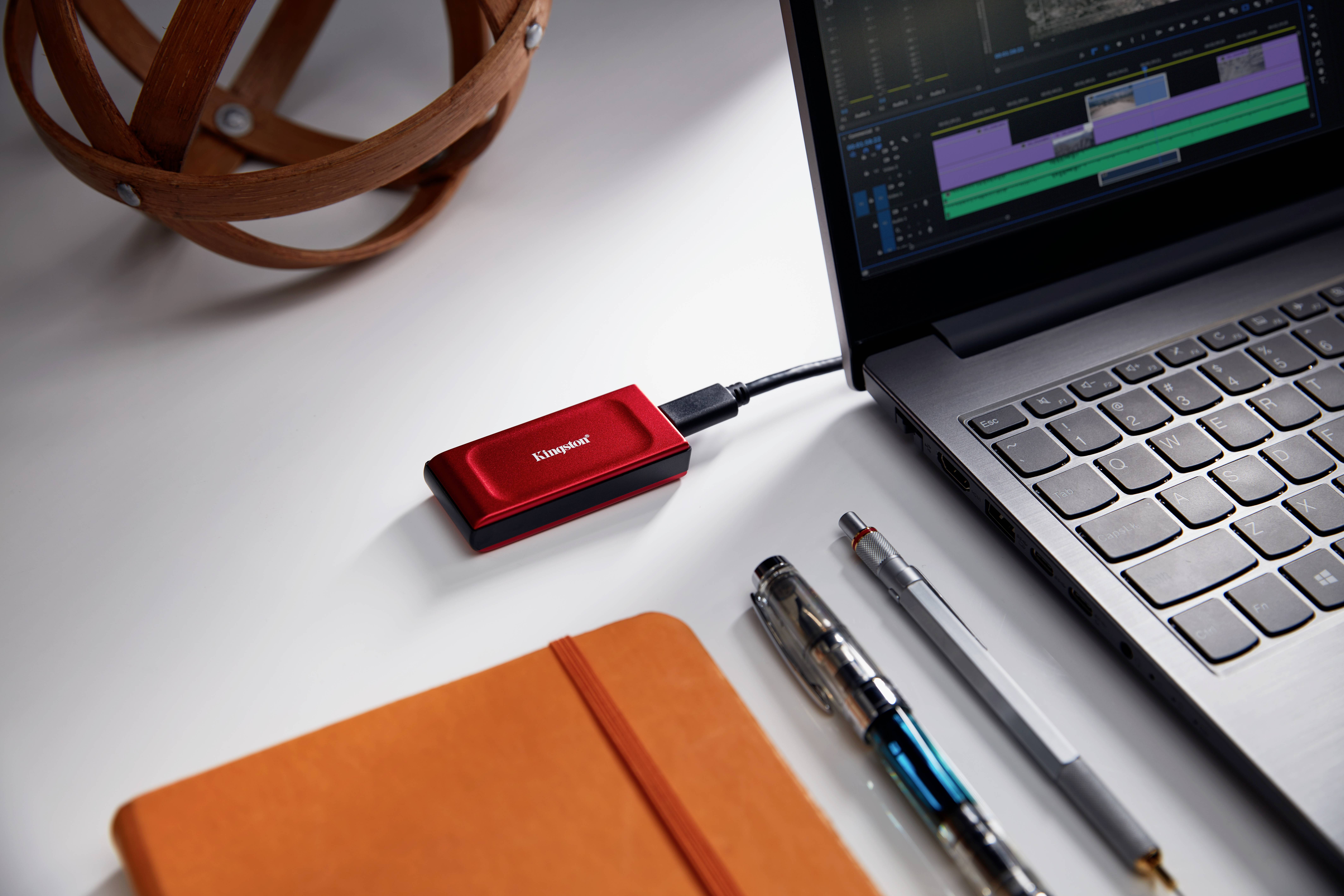 Ein rotes externes Speichergerät ist mit einem Laptop verbunden. Auf dem Laptopbildschirm sind Videobearbeitungsprogramme geöffnet.