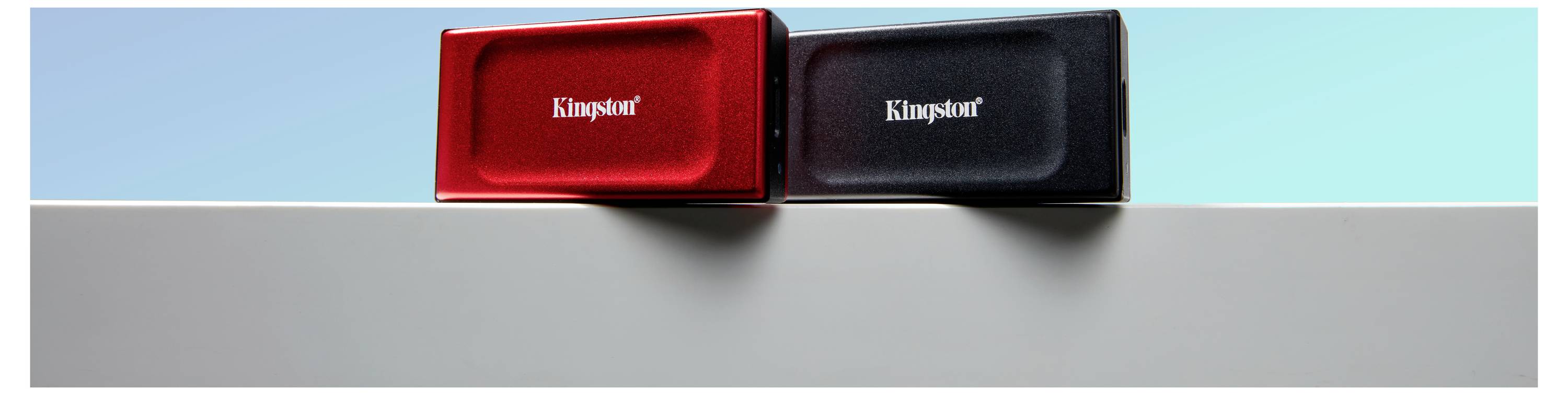 Zwei externe Festplatten in Rot und Schwarz mit der Aufschrift 'Kingston' liegen nebeneinander auf einer grauen Oberfläche vor blauem Hintergrund.