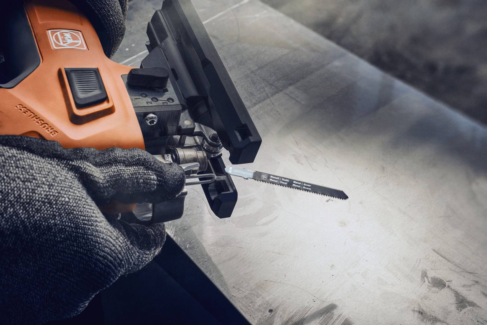 Nahaufnahme einer Person, die eine Stichsäge auf einem Metalltisch hält. Sie trägt Handschuhe und bereitet das Werkzeug zum Schneiden vor.