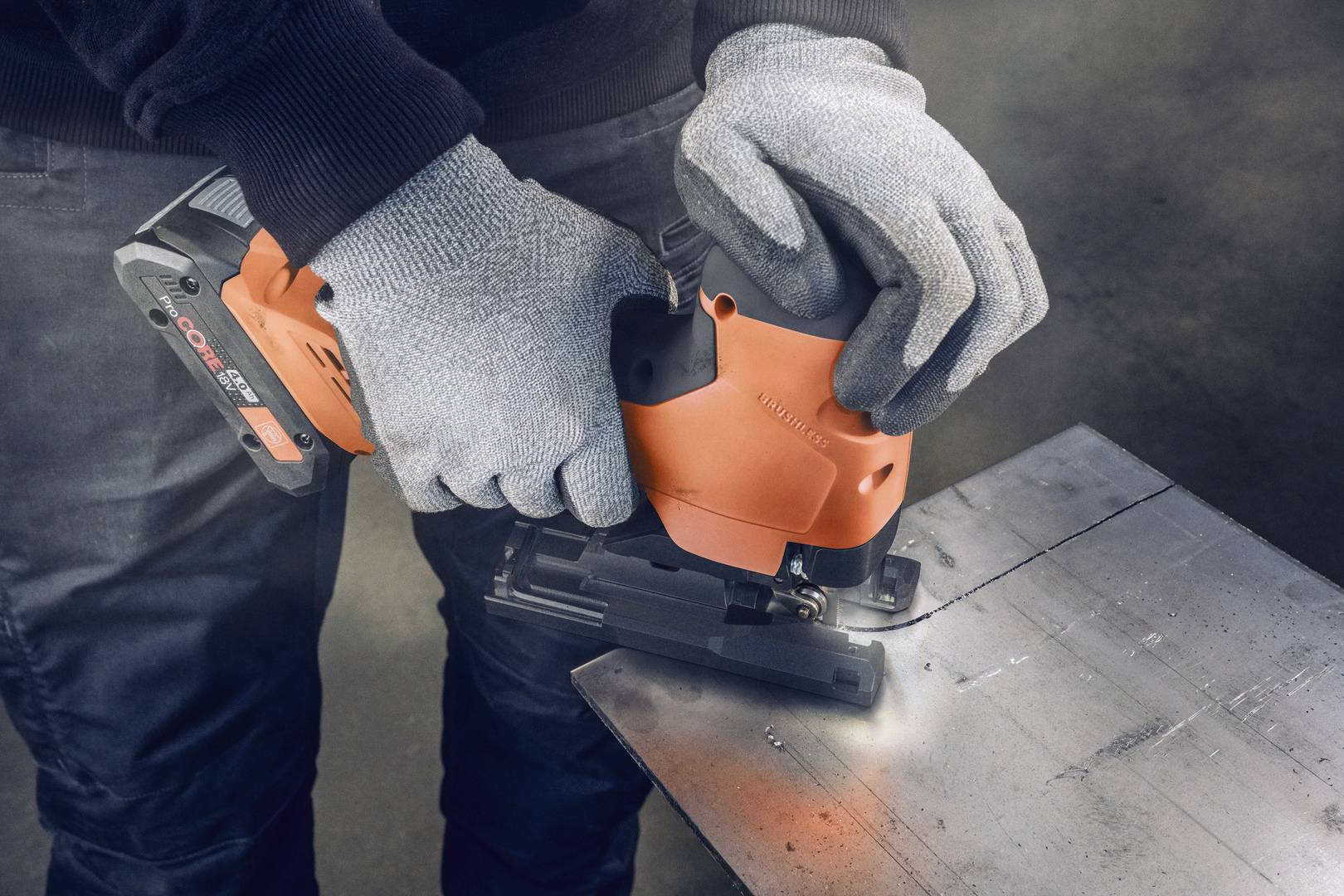 Eine Person trägt Handschuhe und verwendet eine orangefarbene Stichsäge, um ein Metallstück zu schneiden.